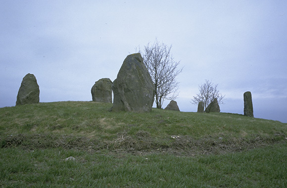 Bilden visar ett antal stenar resta på en svag höjd mot blå himmel.