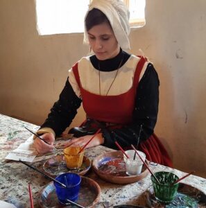 Kvinnlig museilärare i medeltidskläder målar med äggoljefärger.