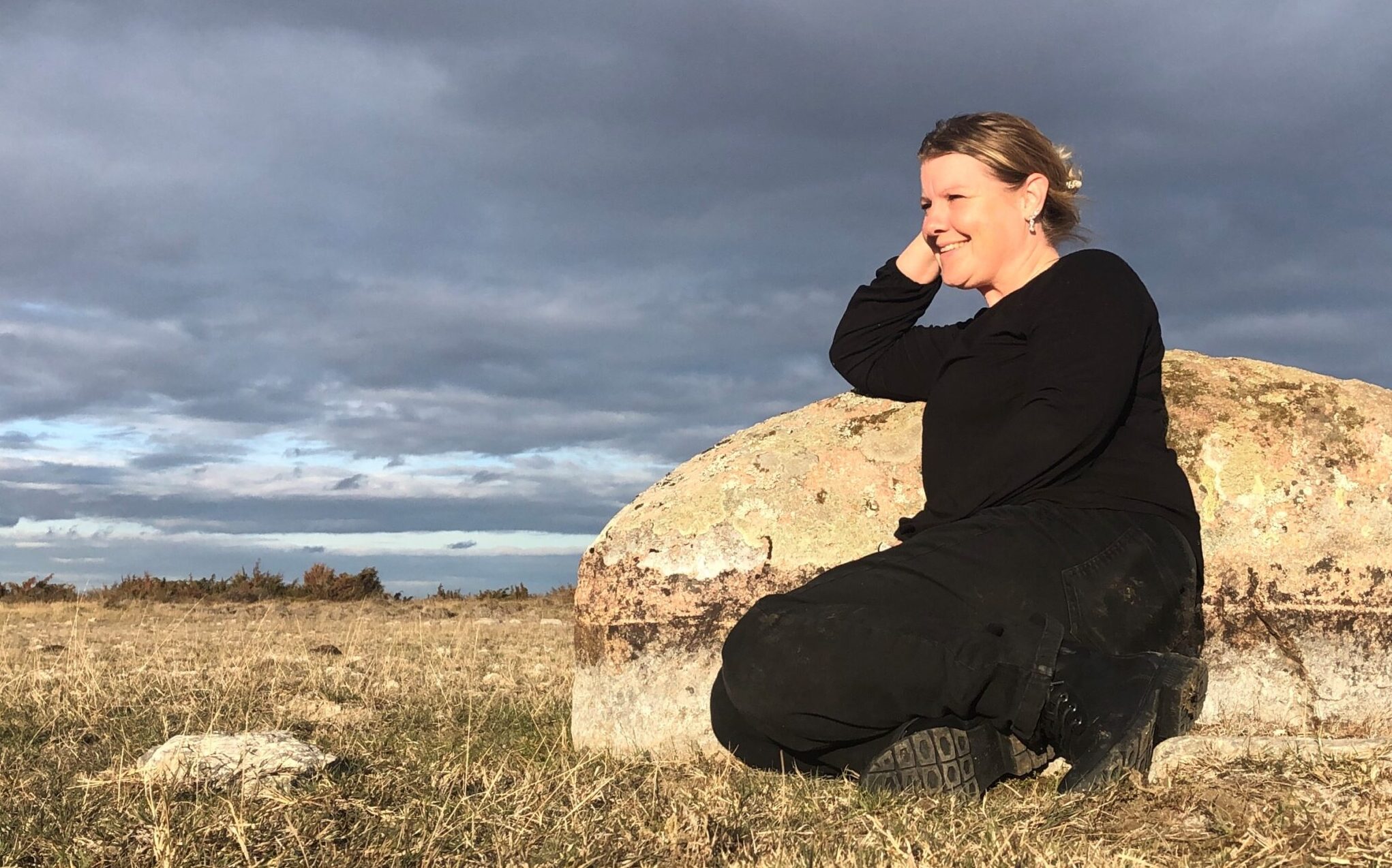 Kvinna sitter vid en sten och blickar ut i landskapet.