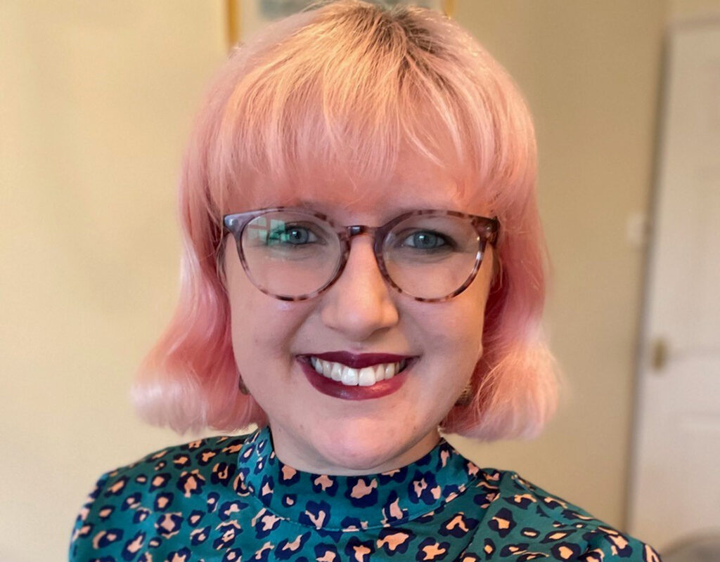En porträttbild på en kvinna med rosa hår och glasögon.