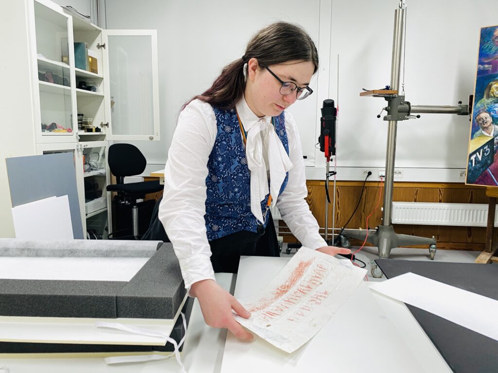 En kvinna håller ett papper med röda detaljer i ett laboratorium.