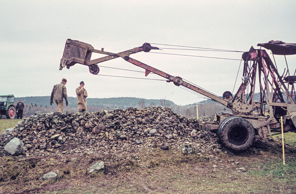 Bild på grävskopa som håller sin skopa ovanför en grav, stensättning