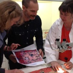 Tre forskare framför ett bord där ett tyg analyseras.