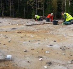 Två arkeologer ligger på knä i ett landskap som liknar ett månlandskap.