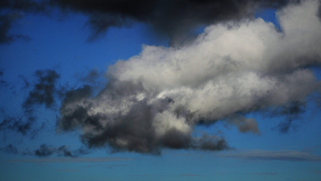 Blå himmel och hav där stora mörka moln hänger över havet.