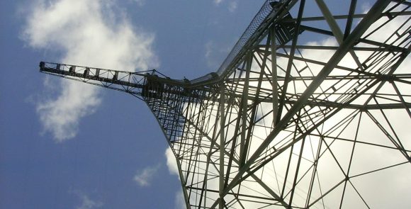 En av radiomasterna i världsarvet Grimeton fotograferad underifrån mot en blå himmel med ett par moln