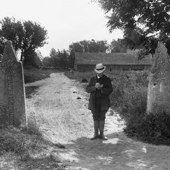 Man med hatt och block i handen står framför medeltida grindstolpar med runor på.