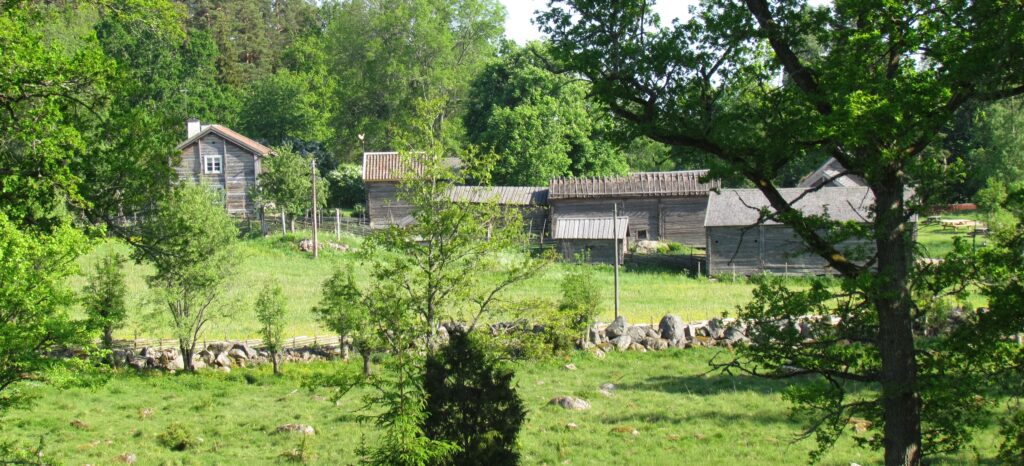 En handfull trähus och bodar i olika storlekar, samlade i en grönskande omgivning.