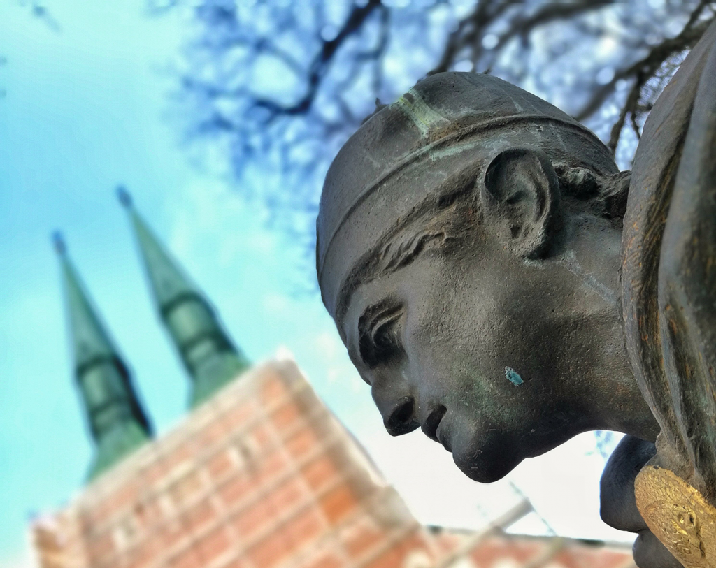 Närbild på staty med kyrkans torn i bakgrunden.