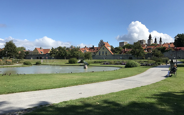 Vy över grönområden med liten sjö i mitten och i bakgrunden tittat husgavlar upp över ringmuren.