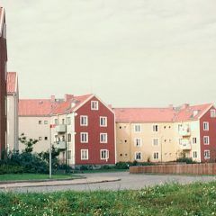 Trevåningshus byggda i vinklar. Grå och gula fasader med röda gavlar, och tegeltak.