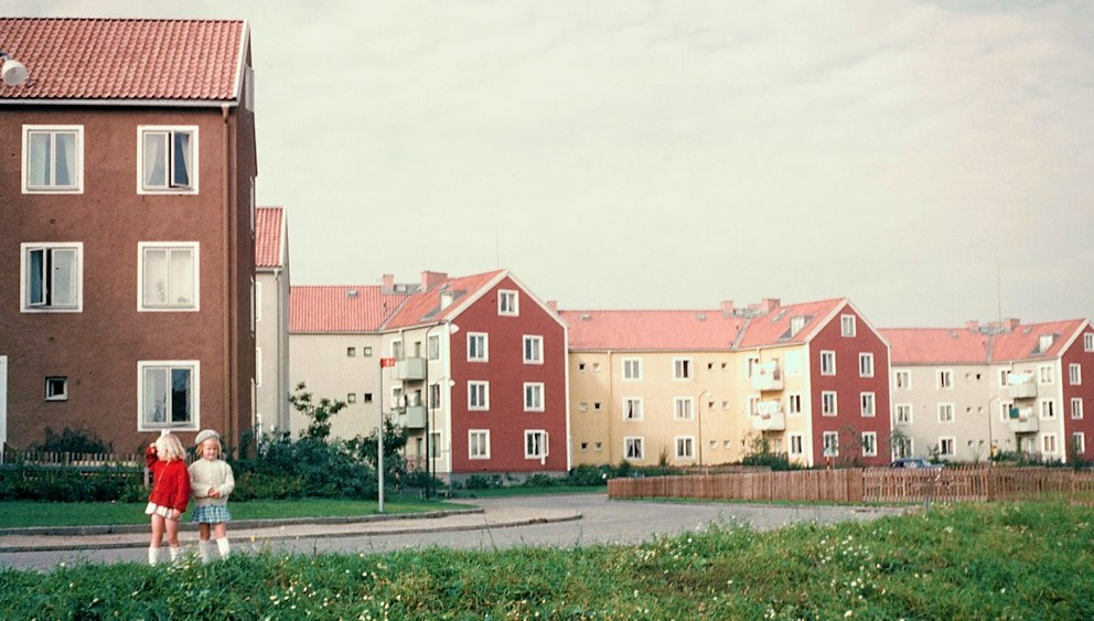 Trevåningshus byggda i vinklar. Grå och gula fasader med röda gavlar, och tegeltak.