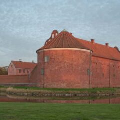 Stor slottsbyggnad i tegel med ett runt citadell på gaveln.