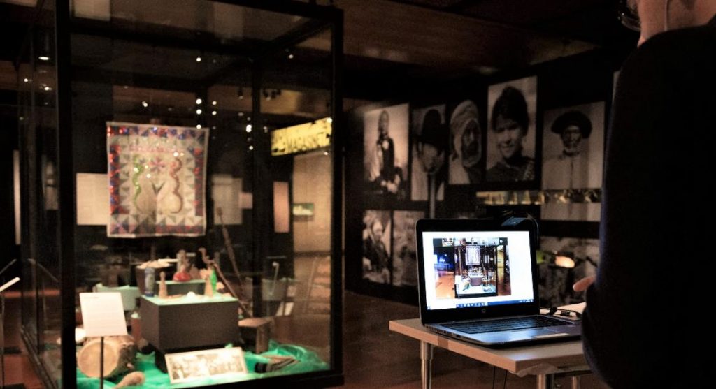 Museimonter med föremål och på bordet framför är en bärbar dator som på skärmen visar en bild av museimontern.