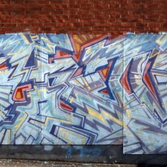 Tegelvägg som målats med stor graffitkonstverk. Blå och gråa toner med gula blixtar i.