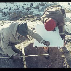 Två personer iklädda mössa i färd med att undersöka en grav under en arkeologisk utgrävning.
