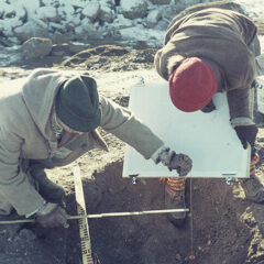 Två personer iklädda mössa i färd med att undersöka en grav under en arkeologisk utgrävning.