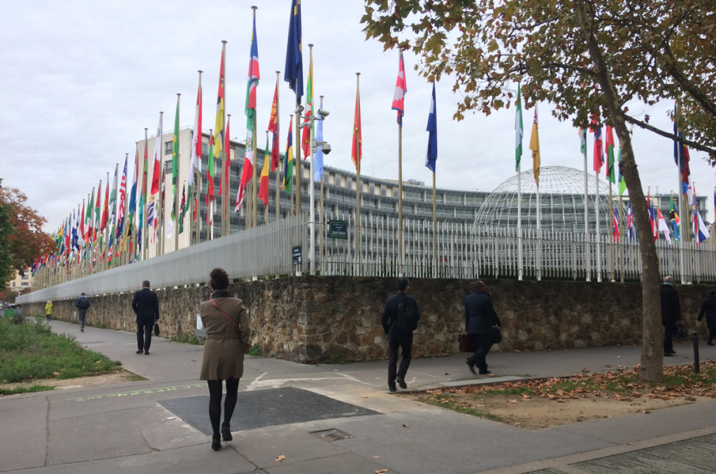 Bilden visar Unescos högkvarter i Paris. På trotoaren går människor och inne på gården hänger hundratals flaggor från världens alla länder