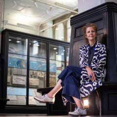 Manchester Museums direktör Esme Ward sitter framför en mörk träpanel i museibyggnaden och ser in i kameran.