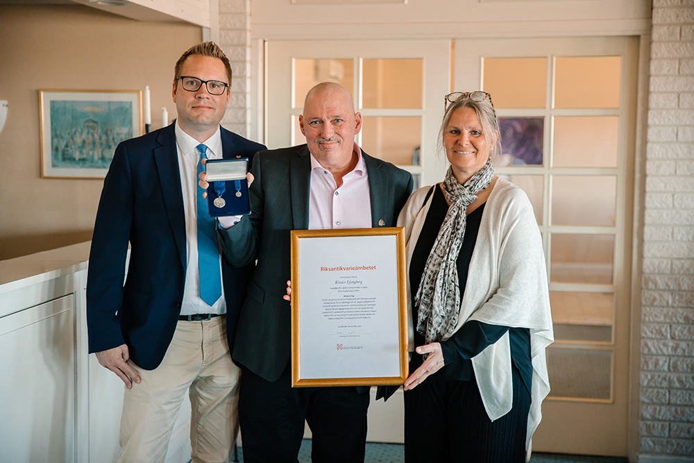 Riksantikvarien Joakim Malmström och överantikvarien Susanne Thedéen, flankerar förtjänstmedaljören Krister Ljungberg som håller upp medalj och diplom.