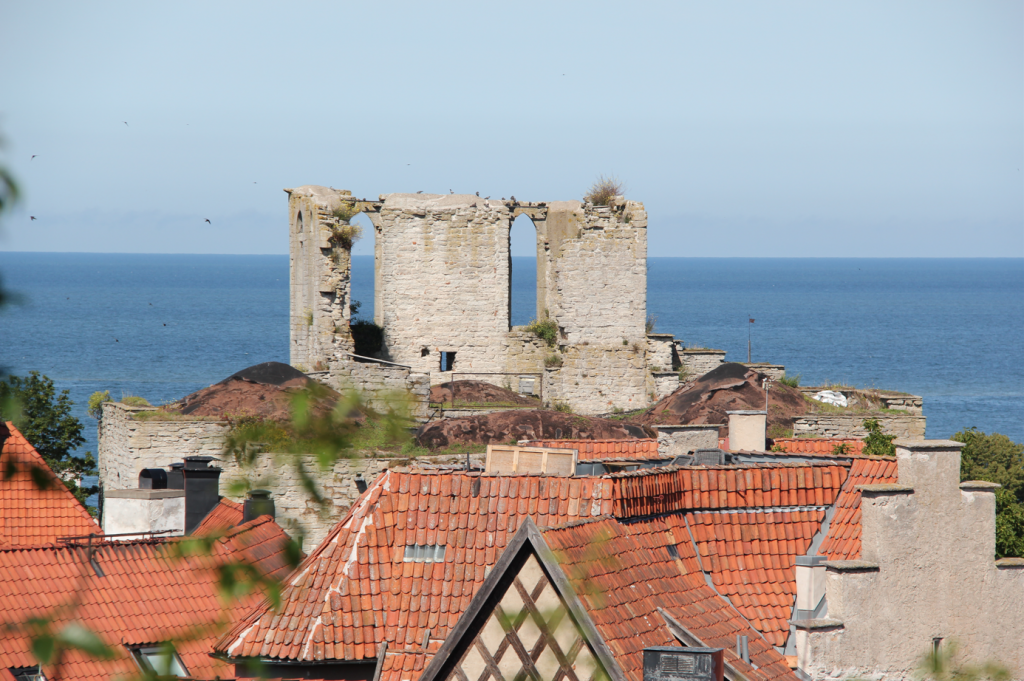 Bilden visar Sankt Lars kyrkoruin i Visby. I förgrunden ser man röda tegeltak och i bakgrunden Östersjön