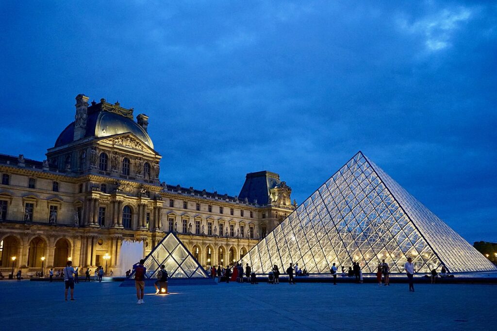 Louvren i skymningen med två glaspyramider i förgrunden.