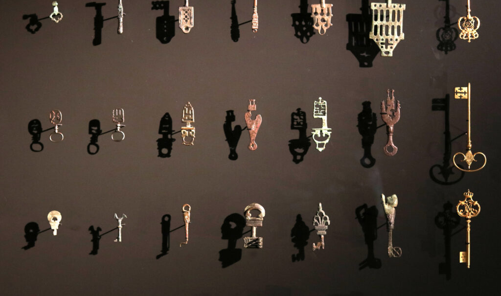 Samling med ett tjugotal olika nycklar i olika material och former,hänger mot en brun bakgrund.