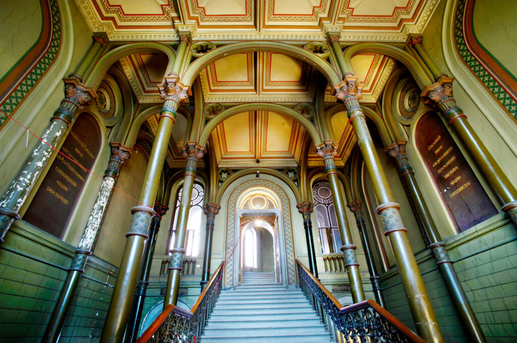 En palatsliknande interiör med trappa, synliga valvbågar och högt till tak.
