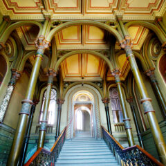 En palatsliknande interiör med trappa, synliga valvbågar och högt till tak.