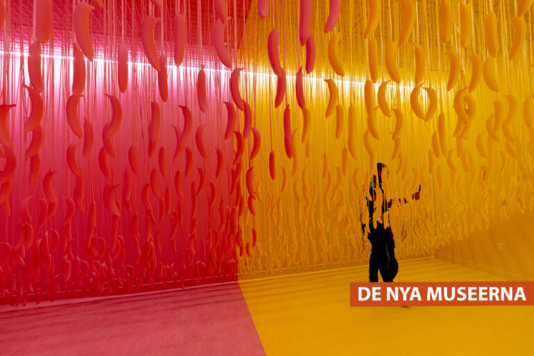 En utställningssal på Museum of Ice Cream i New York, det hänger bananer från taket; en person står och håller i en mobiltelefon.