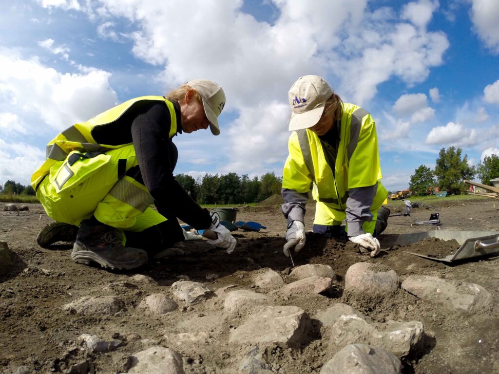 Två arkeologer som gräver runt stenar.