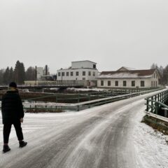 Bro som leder fram till några äldre industribyggnader. I förgrunden går en person mot bron.