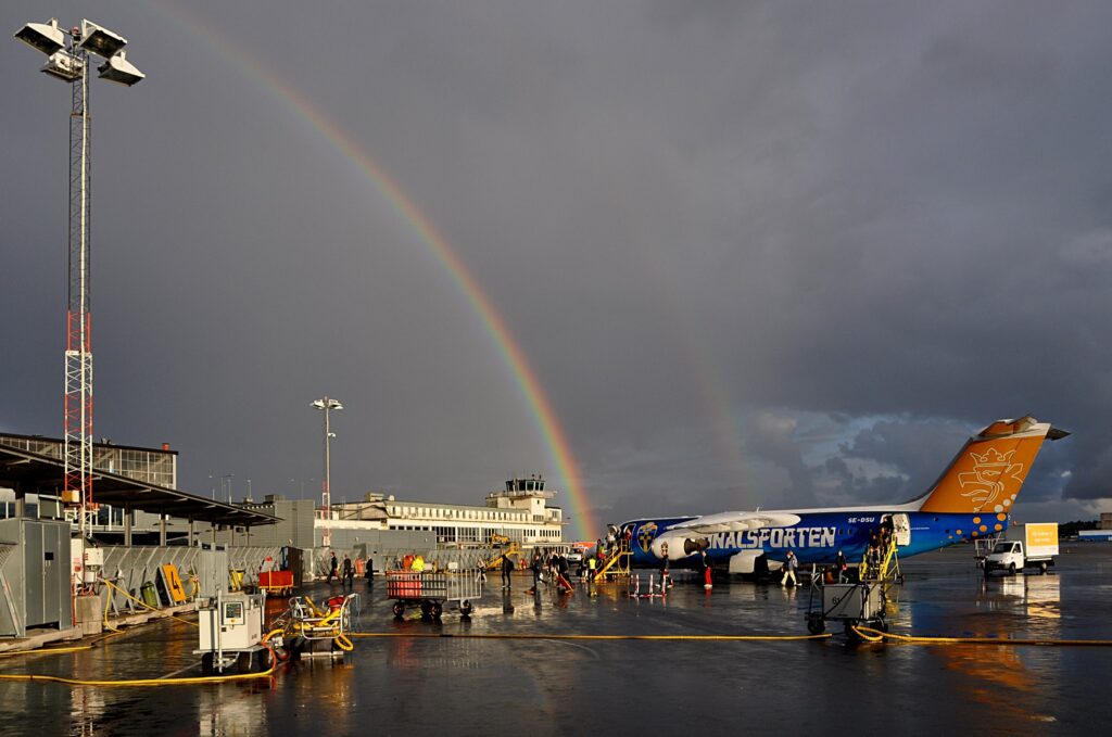 Ett flygplan på en flygplats med en mörk himmel som tornar upp sig med en regnbåge ovanför.