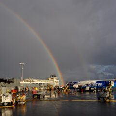 Ett flygplan på en flygplats med en mörk himmel som tornar upp sig med en regnbåge ovanför.