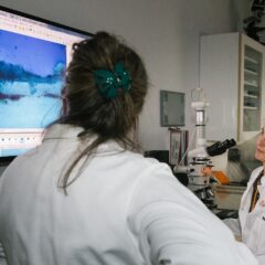Två personer i vita labbrockar vid en datorskärm som visar ett förstorat färgprov i blåaktig ton.