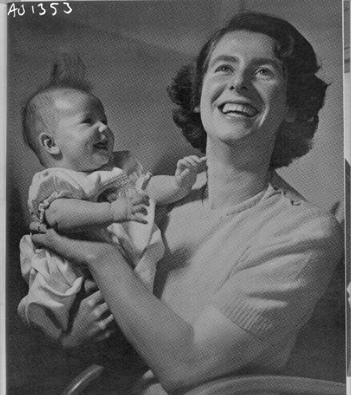 Svartvitt foto där en kvinna håller ett spädbarn i famnen. Båda skrattar glatt.