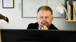 En man sitter med händerna på hakan och tittar på en datorskärm.