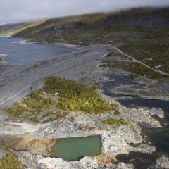 En uppdämd damm som ringlar sig fram, taget med flygfoto. I kanten ser man bergshällen.