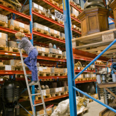 Blå hyllsystem med samlingar och en person uppe på en stege som tittar på samlingarna.