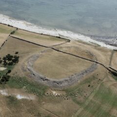 Flygbild över vy där en ringformad upphöjning av marken ligger när strand. Runtom ligger åkrar.