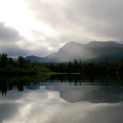 Sjö med stort bergmassiv i bakgrunden som speglas i sjön, därovan en dramatisk vacker himmel med mörka moln.