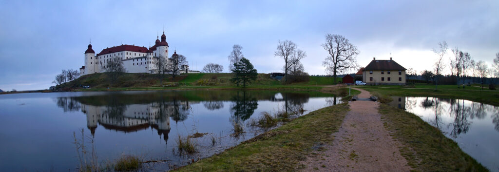 Ett vitt slott med tre höga, runda torn på en kulle vid sjön, slottet har sin spegelbild i vattnet. En smal stig leder fram till ön.