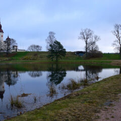Ett vitt slott med tre höga, runda torn på en kulle vid sjön, slottet har sin spegelbild i vattnet. En smal stig leder fram till ön.