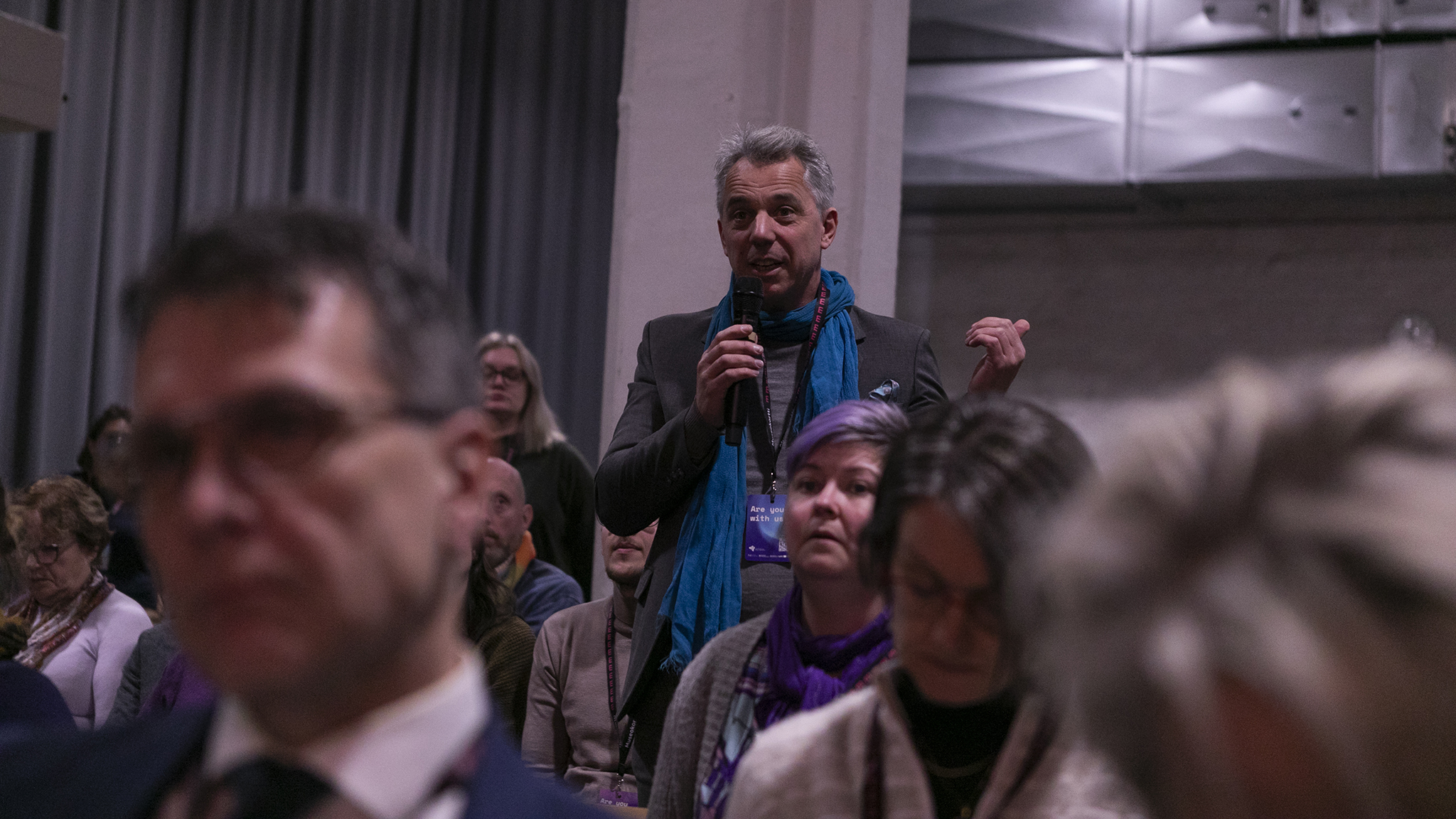 En man står i publiken på en konferensens och talar i en mikrofon.