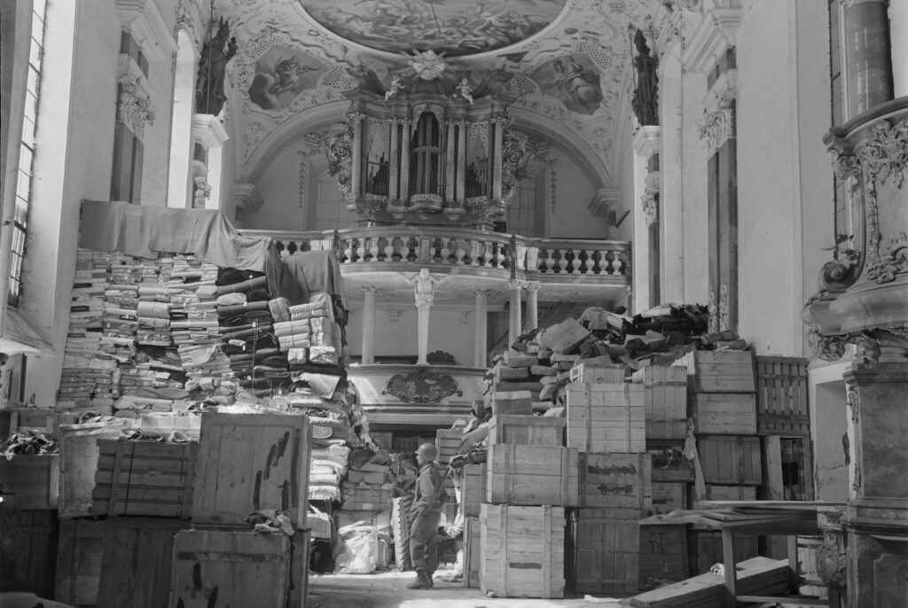 Svartvit bild inifrån en kyrka fylld med lådor, i bakgrunden altaret och i mitten står en soldat iklädd hjälm.