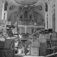 Svartvit bild inifrån en kyrka fylld med lådor, i bakgrunden altaret och i mitten står en soldat iklädd hjälm.