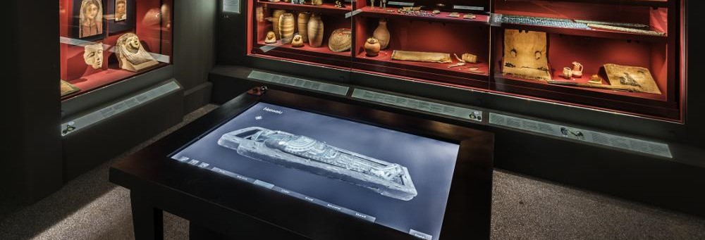 Monter med krukor och andra museiföremål. I förgrunden en röntgenbild på en digital skärm i ett bord.