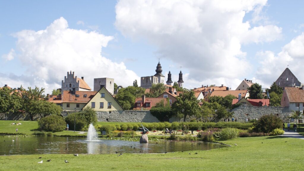 Vy över grönområden med liten sjö i mitten och i bakgrunden tittat husgavlar upp över ringmuren.