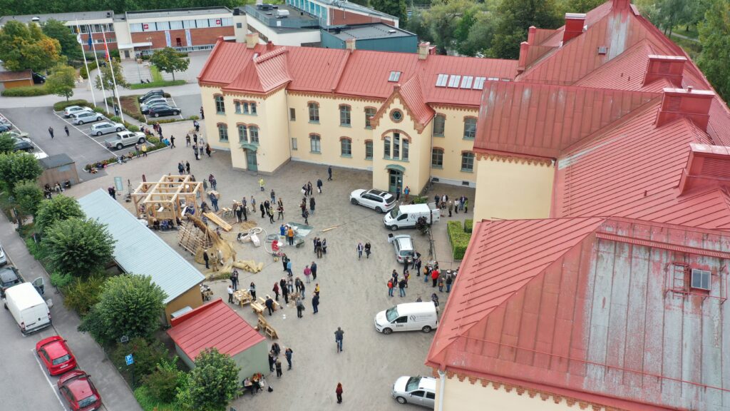 En drönarbild på en äldre byggnad tagen ovanifrån, med en massa människor som rör sig på gården kring huset.
