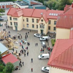 En drönarbild på en äldre byggnad tagen ovanifrån, med en massa människor som rör sig på gården kring huset.